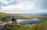 Man sits on a rock and looks at Llyn y Fan Fach lake. Brecon Beacons National Park. Black Mountain, Carmarthenshire, South Wales, the United Kingdom.
