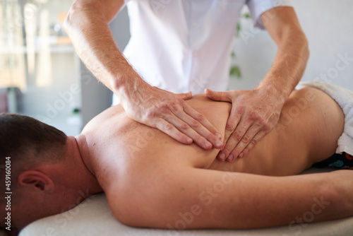 Closeup of man massaging his client's back with his hands in massage cabinet