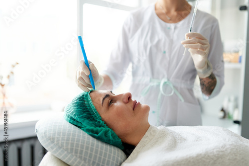 Cosmetologist draws points for a beauty injection on the woman s face. Preparation for a cosmetic anti-aging procedure.
