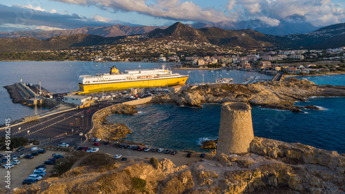 Aerial view of the lighthouse on Pietra island with a yellow ferry moored in the port of Île Rousse in the background, Upper Corsica, France - Picturesque harbour on small islets photo