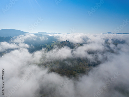 A thin morning fog covers the Ukrainian mountains. Green grass on the slopes of the mountains. A curly thin fog spreads over the mountains. Aerial drone view.