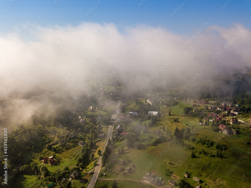 Thin morning fog over a mountain village. Fog covers the Ukrainian slopes of the mountains. Aerial drone view.