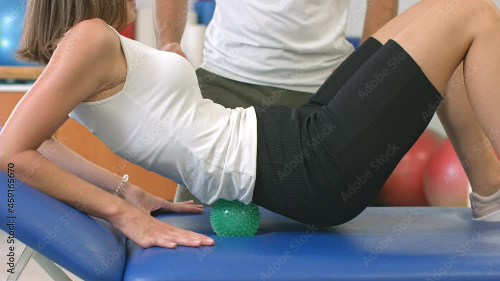 Handheld shot of a Caucasian male physiotherapist and female patient during physical therapy for low back with a spiky massage ball. Handheld shot of a Caucasian male physiotherapist and female patient during physical therapy for low back with a spiky massage ball.