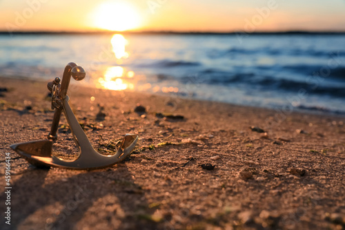 Fototapet Metal anchor on shore near river at sunset