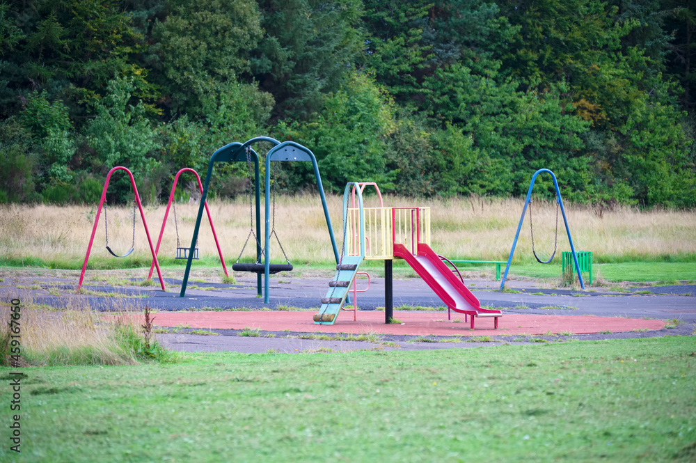 Fototapeta premium Empty playground derelict swings and slide in rural area