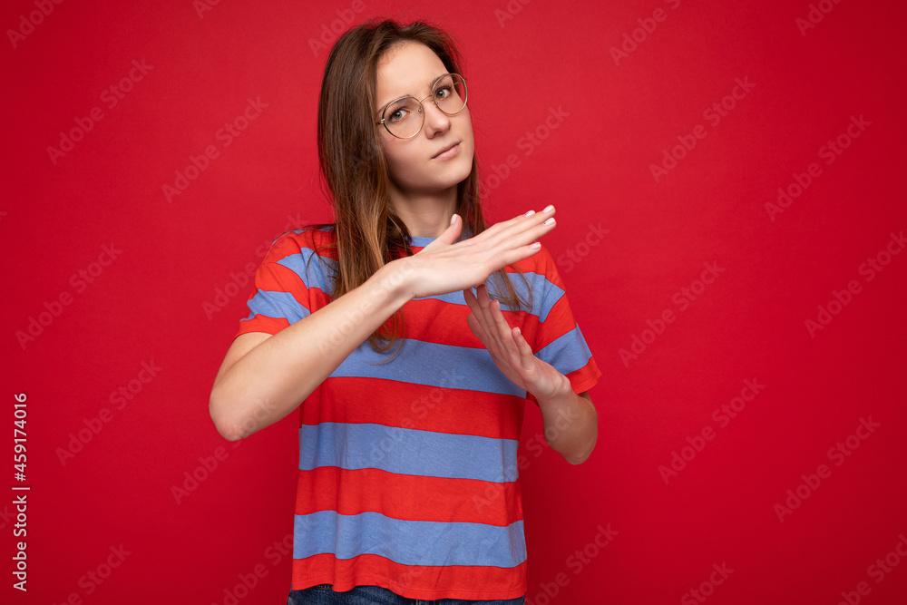 Portrait of strict young cool attractive brunette woman with sincere emotions wearing trendy striped t-shirt and optical glasses isolated over red background with copy space and showing timeout Portrait of strict young cool attractive brunette woman with sincere emotions wearing trendy striped t-shirt and optical glasses isolated over red background with copy space and showing timeout