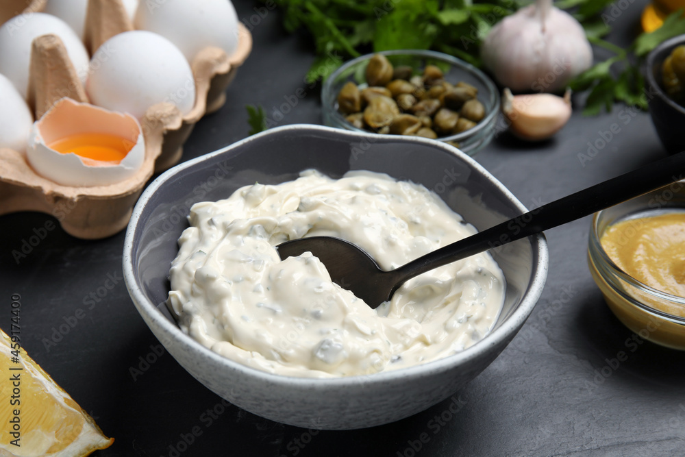 Tasty tartar sauce and ingredients on black table Tasty tartar sauce and ingredients on black table