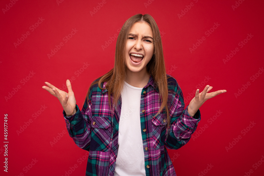 Portrait of young dissatisfide angry emotional attractive dark blonde female person with sincere emotions wearing stylish violet check shirt and white t-shirt with empty space isolated over red Portrait of young dissatisfide angry emotional attractive dark blonde female person with sincere emotions wearing stylish violet check shirt and white t-shirt with empty space isolated over red