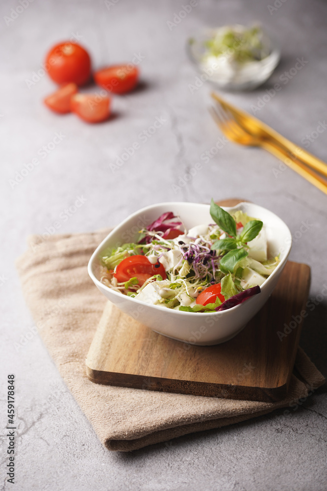 A small white salad bowl with microgreens, cherry tomatoes and fresh basil leaves on a wooden board on a grey concrete surface A small white salad bowl with microgreens, cherry tomatoes and fresh basil leaves on a wooden board on a grey concrete surface