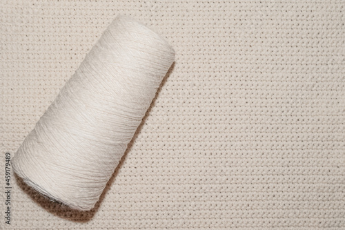 Beige spool of thread on the knitted napkin background
