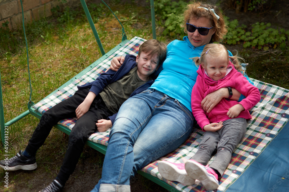Grandmother and her two grandchildren having fun on a swing, Grandson and granddaughter relaxing outdors in grandma countryside house.