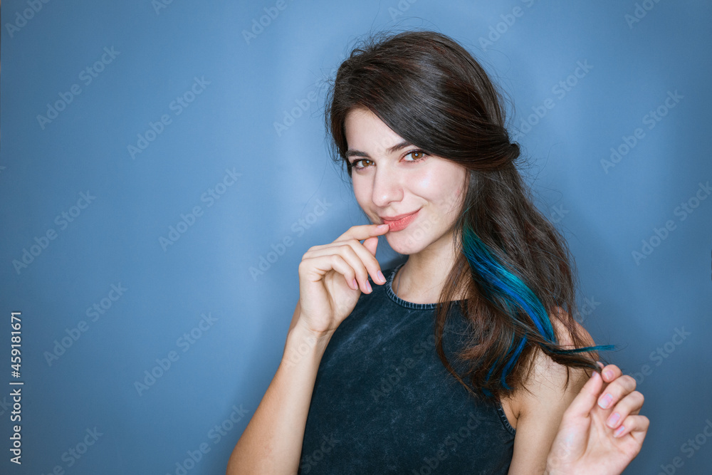 Image of a happy young lady standing isolated on a blue background. Looking camera holding finger to mouth and smiling cute Image of a happy young lady standing isolated on a blue background. Looking camera holding finger to mouth and smiling cute
