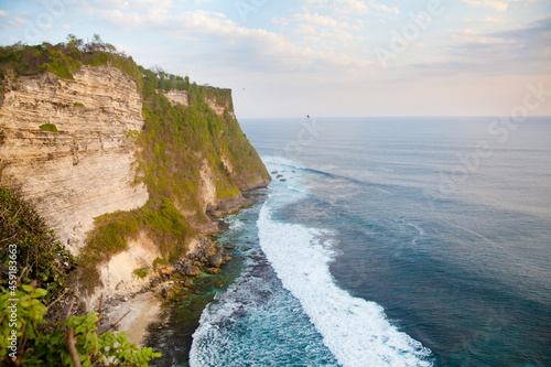 View of Uluwatu cliff with blue sea in Bali, Indonesia. Rocky cliff and sea waves at sunset.