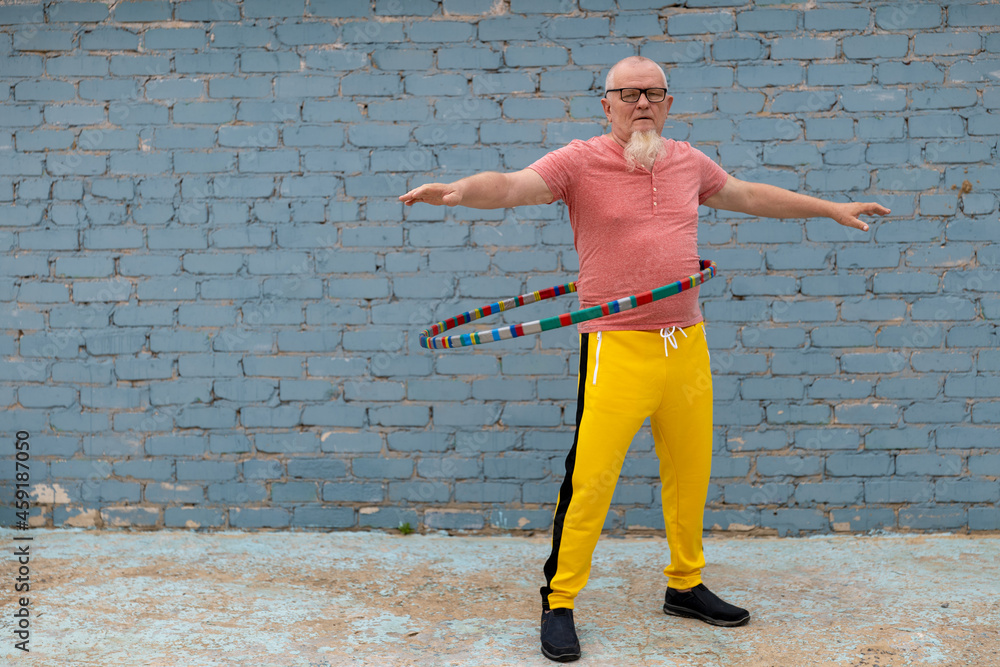 elderly man in yellow sweatpants spinning hoop on playground in front of house. Outdoor sports elderly man in yellow sweatpants spinning hoop on playground in front of house. Outdoor sports