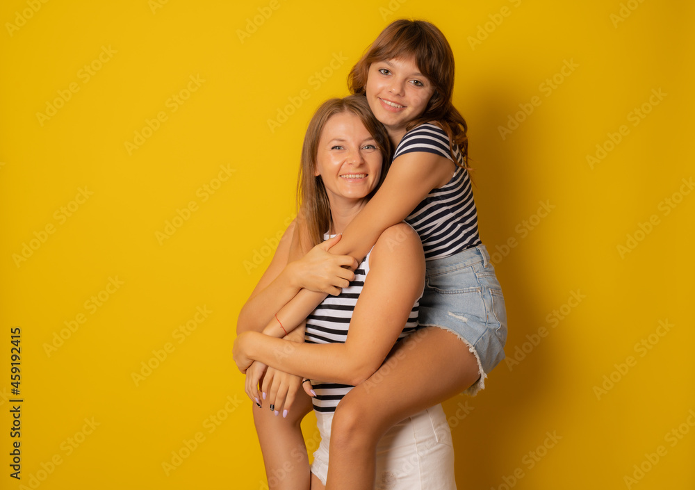 Togetherness Concept. Daughter hugging her mum from the back, showing her love, yellow studio wall Togetherness Concept. Daughter hugging her mum from the back, showing her love, yellow studio wall