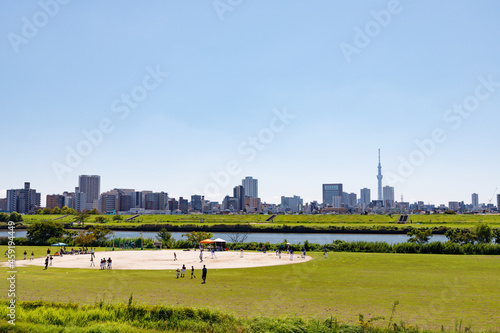 青空を背景に足立区側から見た荒川区方面の景色と河原のグランドで野球をする人々 photo
