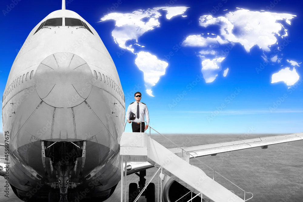 Airplane Captain posing in front of movable boarding ramp near the entrance to the passenger airplane with clouds in shape of world map concept for transportation around the world