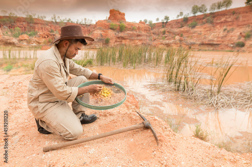 Photography Gold digger in retro clothes washed gold in sieve used for screening in lake with rocky bank