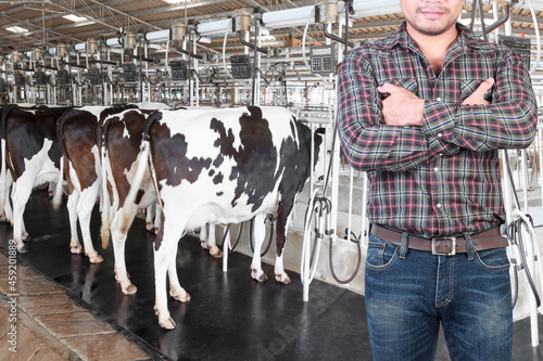 Farmer standing cross one's arm proud in front of cow milking facility and mechanized milking equipment in a modern farm photo