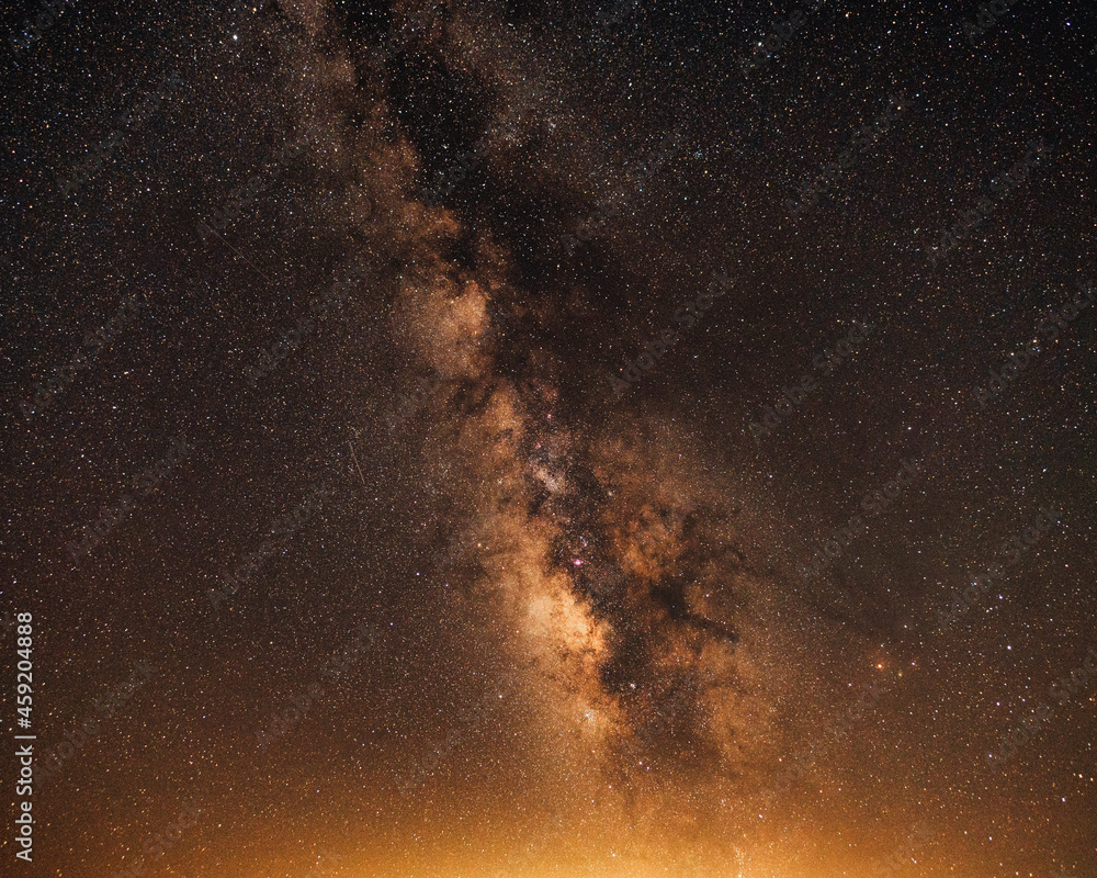 Orange sky with milky way galaxy and light pollution from a distant city