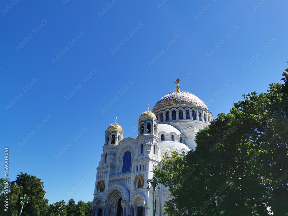 St. Nicholas Cathedral among the trees against the background of a cloudless sky, on a summer day in Kronstadt.