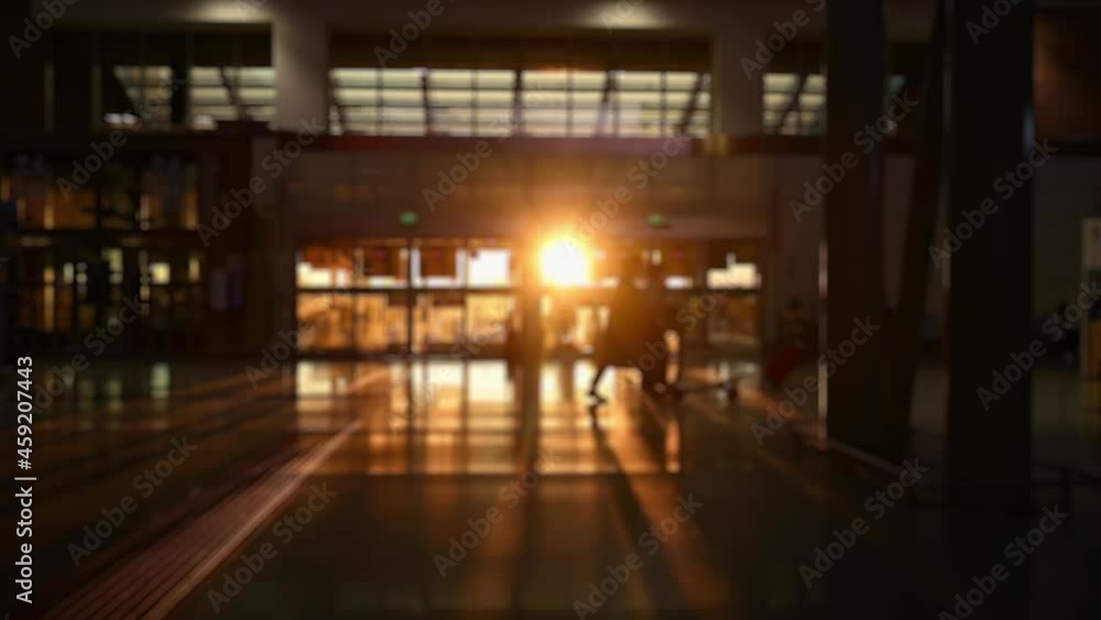 (Defocused video) Blurred silhouette of some tourists walking inside an airport terminal during a stunning sunset. Travel concept during the Covid-19 pandemic. (Defocused video) Blurred silhouette of some tourists walking inside an airport terminal during a stunning sunset. Travel concept during the Covid-19 pandemic.