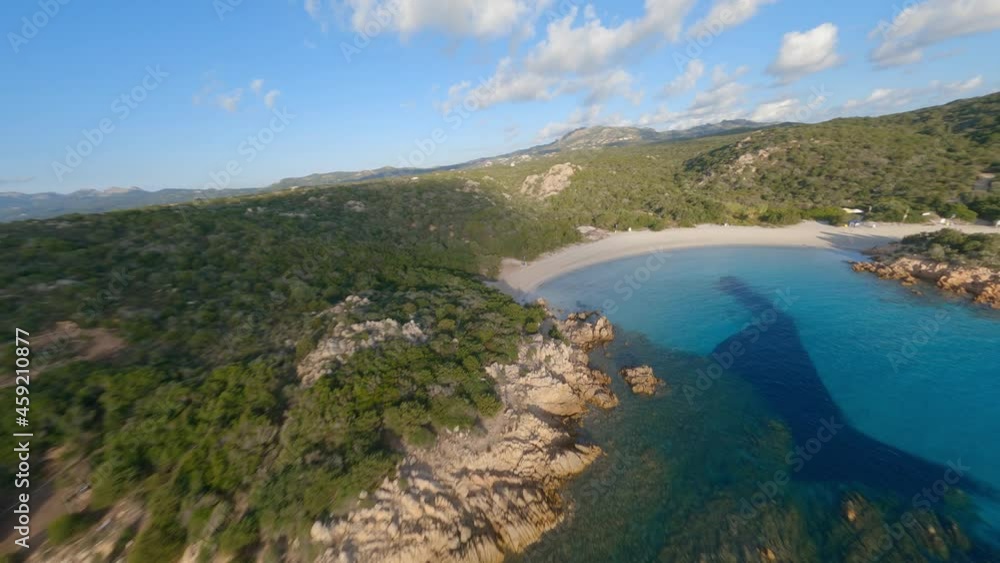 FPV video, view from above, aerial view from an FPV drone flying at high speed over a green coast with a beautiful white sand beach bathed by a turquoise water. Prince Beach (Spiaggia del Principe) FPV video, view from above, aerial view from an FPV drone flying at high speed over a green coast with a beautiful white sand beach bathed by a turquoise water. Prince Beach (Spiaggia del Principe)