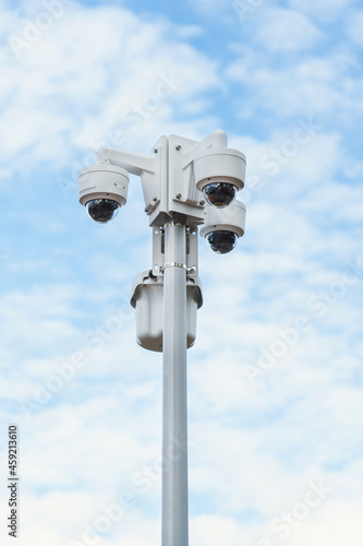 A group of CCTV cameras on a pole against the background of the sky with clouds