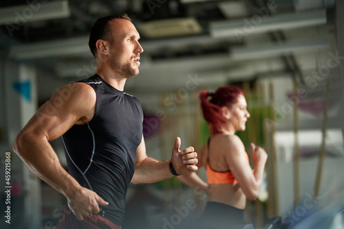 Muscular build athlete runs on treadmill in gym.