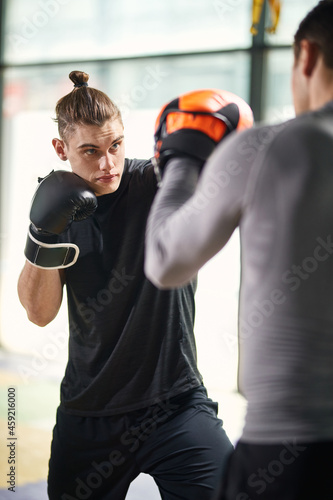 Athletic man practices boxing with his instructor at gym.