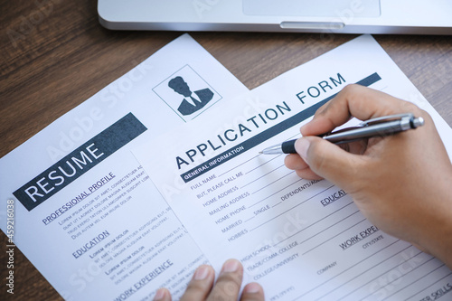 Closeup hand holding pen for completing the application form with resume on the table