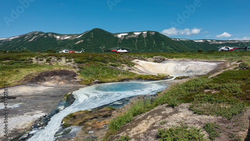 A thermal spring in the caldera of an extinct volcano. There are sulfur deposits on the soil. Picturesque mountains against the blue sky. In the distance, you can see parked helicopters. Kamchatka.  © Вера 