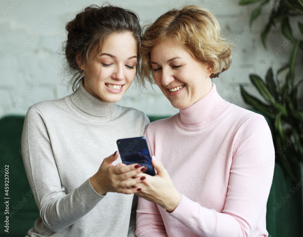 Family, people and technology concept: Aged woman and her adult daughter using smartphone at home Family, people and technology concept: Aged woman and her adult daughter using smartphone at home