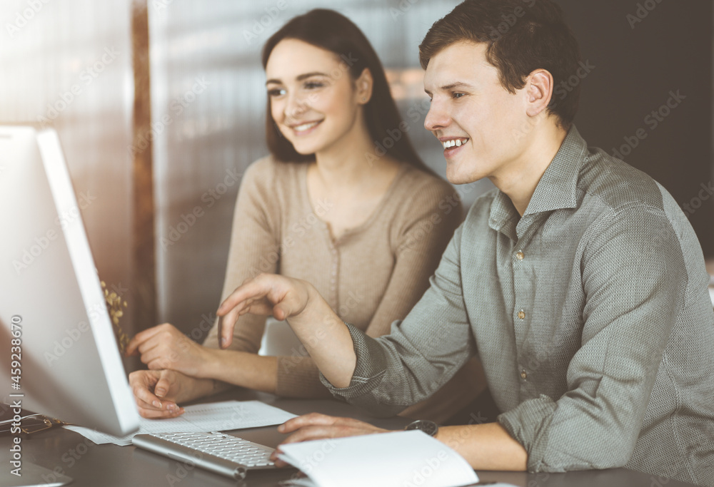 Handsome young businessman is looking at camera with a smile, while sitting together with female colleague in sunny office Handsome young businessman is looking at camera with a smile, while sitting together with female colleague in sunny office
