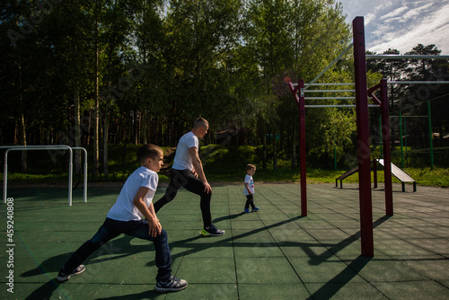 Caucasian man and two boys doing exercises outdoors. Father and sons train on the sports ground