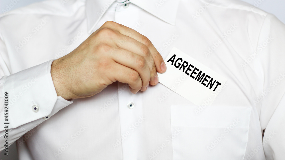 A businessman in a white shirt shows a business card with text AGREEMENT , copy space, business concept A businessman in a white shirt shows a business card with text AGREEMENT , copy space, business concept