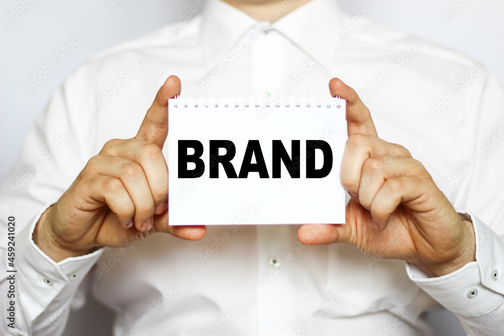 A businessman in a white shirt shows a business card with text BRAND, copy space, business concept A businessman in a white shirt shows a business card with text BRAND, copy space, business concept