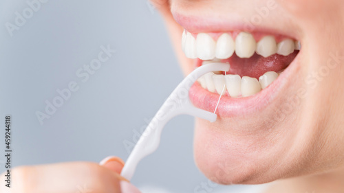 Caucasian woman brushing teeth with toothpick with dental floss on white background. photo