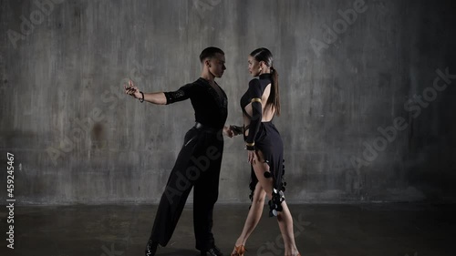 The young active millennial dance ballroom couple in black dress dancing in sensual pose over studio background. Professional dancers dancing latino. Hobby dance concept. Human emotions, love passion