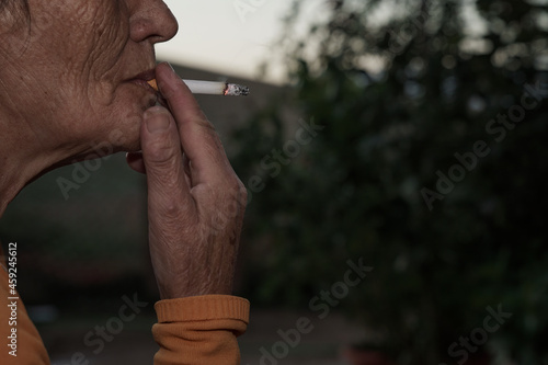 Detalle de mujer fumando tabaco con manchas en la piel y envejecida prematuramente a causa del tabaco aspirando el cigarro. 