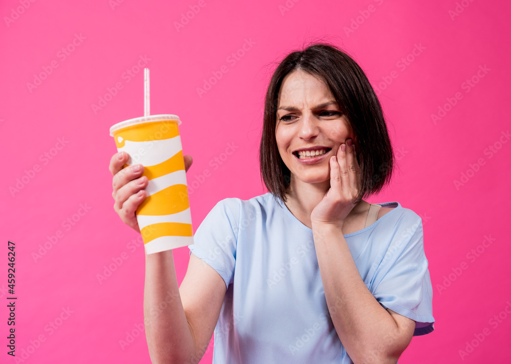Young woman with sensitive teeth drinking cold water on color background Young woman with sensitive teeth drinking cold water on color background