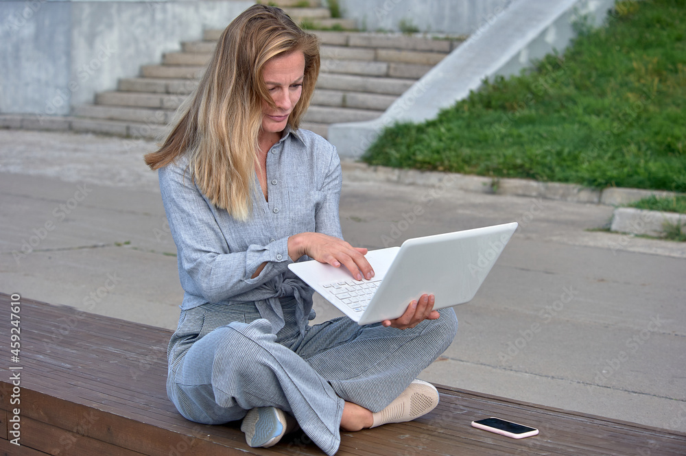 A woman with a laptop sits on a wooden platform, works online A woman with a laptop sits on a wooden platform, works online