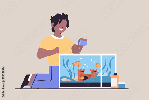 african american boy feeding fishes in aquarium domestic animal friendship with pet concept horizontal