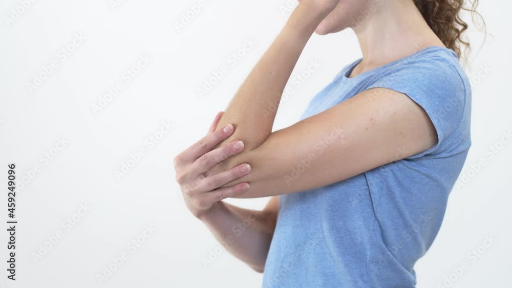 Woman stands on white background and rubs her sore elbow, side view