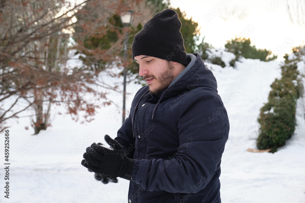 Young caucasian man making a snowball in a park.