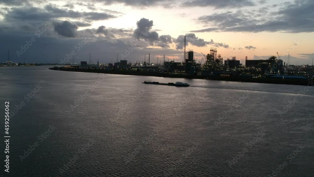 Industrial barge sailing near Antwerp harbor buildings, aerial drone view