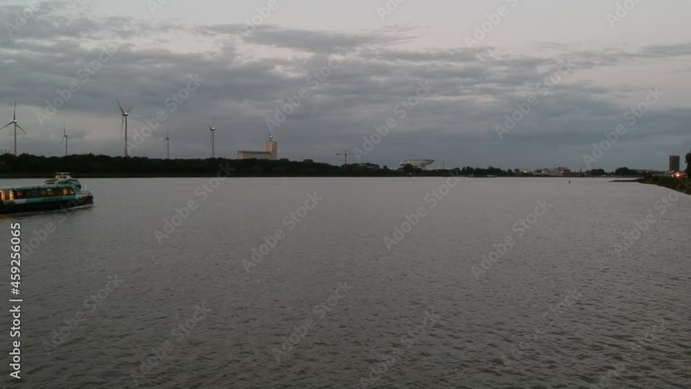 Transport boat passing by near industrial buildings of Antwerp port with windmills