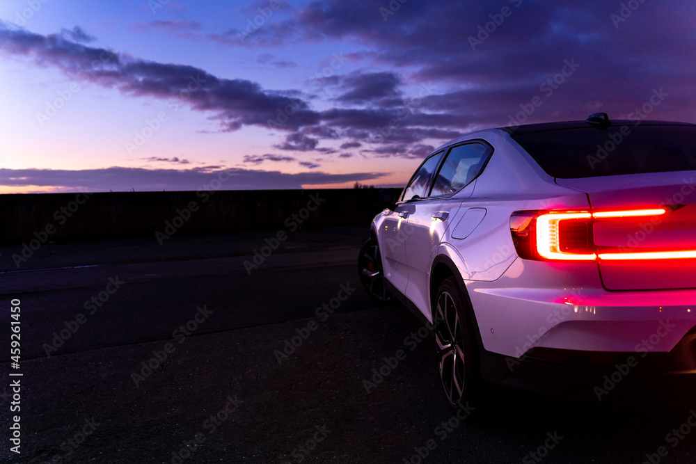 Sunset with purple cloudy sky with white sports car on the right side
