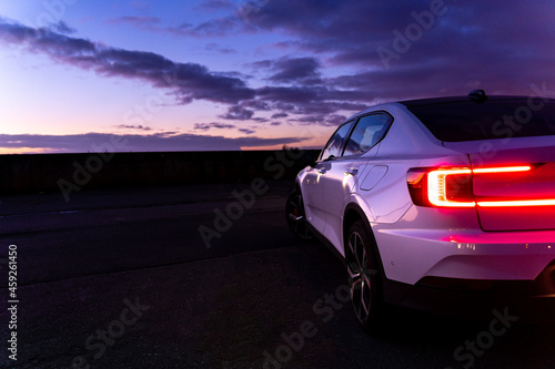 Sunset with purple cloudy sky with white sports car on the right side © Arjan