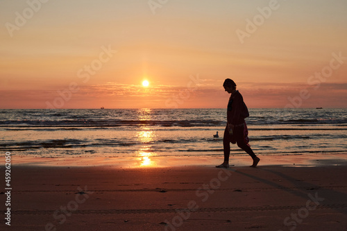 A silhouette of a person walking on a sea shore at sunset